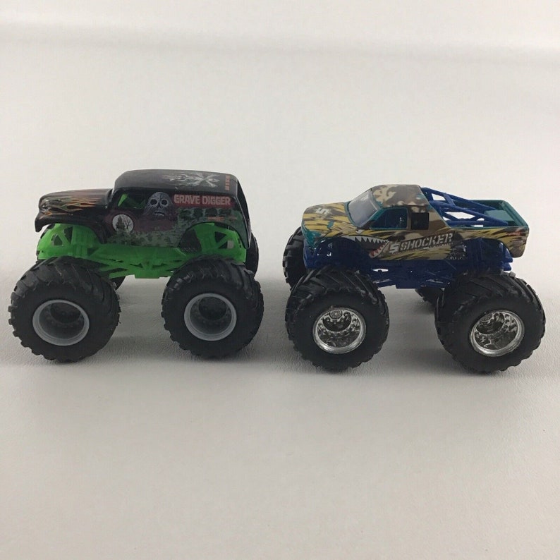 May include: Two monster truck toys, one green and black with "Grave Digger" written on the side, and the other blue and green with "Shockwave" written on the side.