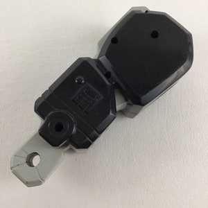 May include: A black and gray plastic toy weapon with a handle and a blade. The blade is shaped like a rectangle with a rounded edge. The handle is shaped like a cylinder with a hole in the center. The toy weapon is made of two pieces that are connected together.