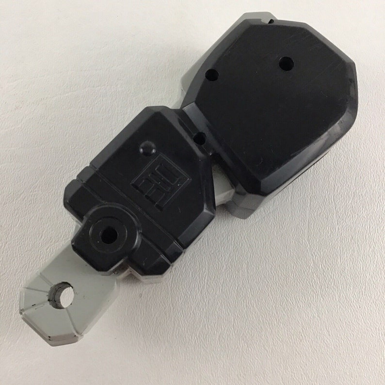 May include: A black and gray plastic toy weapon with a handle and a blade. The blade is shaped like a rectangle with a rounded edge. The handle is shaped like a cylinder with a hole in the center. The toy weapon is made of two pieces that are connected together.