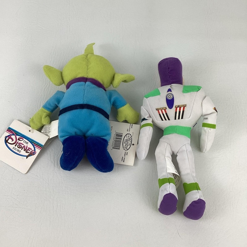 Pu&ograve; includere: Due peluche di The Disney Store. Uno &egrave; un alieno verde a tre occhi con tuta blu e colletto viola. L'altro &egrave; un personaggio ranger spaziale bianco, verde e viola con un design a jetpack sul retro. Entrambi hanno le etichette attaccate.