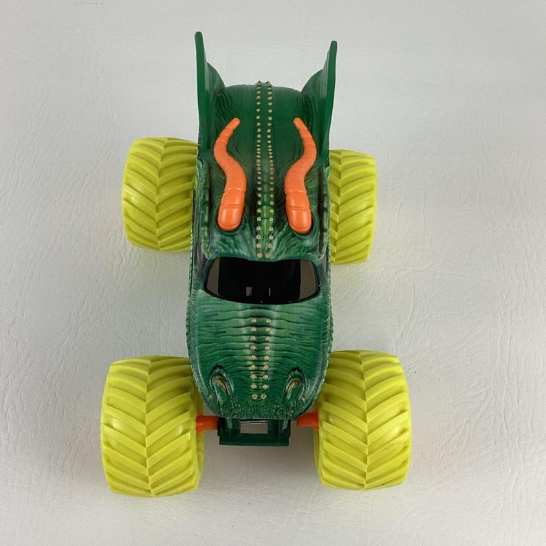 Pu&ograve; includere: Camion mostro giocattolo verde con pneumatici gialli. Il camion presenta un design a forma di drago con accenti arancioni e un parabrezza nero. I pneumatici sono grandi e hanno un motivo a spina di pesce.