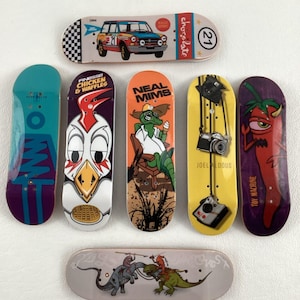 Puede incluir: Siete mini-skateboards con varios diseños. Los diseños incluyen un pollo de dibujos animados, un cocodrilo verde, una cámara, un chile, un coche y dos diseños abstractos. Los skateboards están hechos de madera y tienen una variedad de colores.