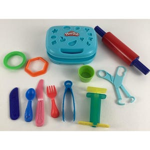 May include: A Play-Doh playset with various tools and accessories. Includes a blue container with shape cutouts, a red rolling pin, and several colorful plastic tools like scissors, a fork, and a knife. The set is designed for creative play.