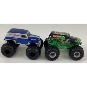 May include: Two toy monster trucks. One is blue and silver with "Grave Digger" text. The other is green and black with "Grave Digger" text and a skull graphic. Both have large black tires.