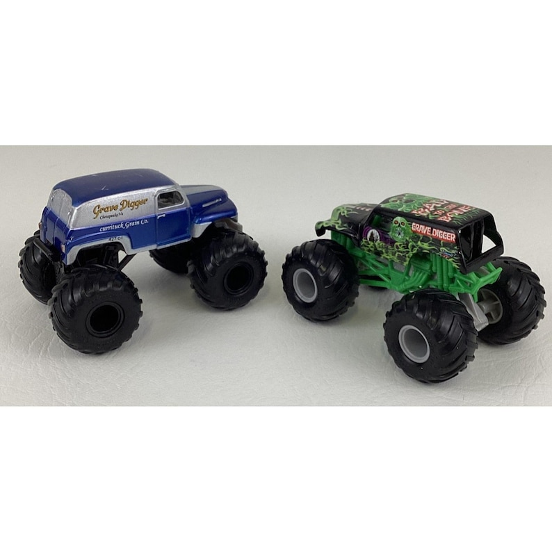 May include: Two toy monster trucks. One is blue with "Grave Digger" text, the other is green and black with "Grave Digger" text. Both have large black tires and are on a white background.