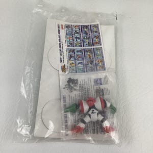 May include: A Z-Bots action figure in a clear plastic bag with a white cardboard backing. The robot is white with red and green accents and a black Z logo on its chest. An instruction sheet with a grid of various robot characters is included.