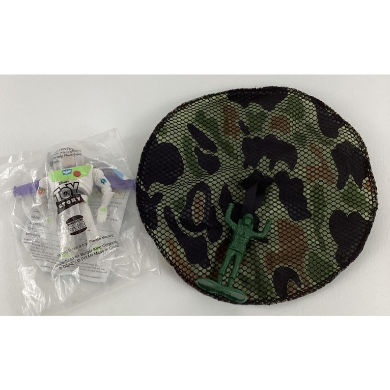 May include: A clear plastic package containing a Buzz Lightyear action figure with the words "Toy Story" printed on the front. Next to it is a green camouflage net with a green plastic toy soldier.