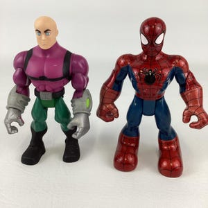 May include: Two action figures: one of Lex Luthor in purple and green, and one of Spider-Man in red and blue. Lex Luthor has a bald head and gray gloves. Spider-Man has a black spider emblem on his chest.