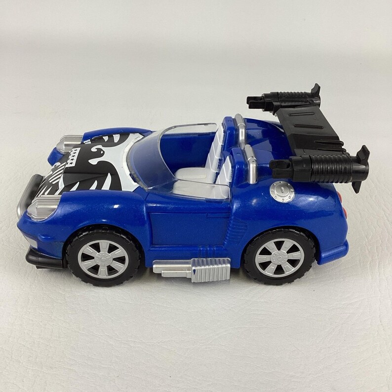 May include: A blue toy car with a black spoiler and silver wheels. The car has a white and black design on the hood and a clear windshield. The toy car is a convertible.