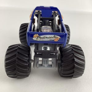 May include: A blue monster truck toy with large black tires. The truck has a blue body with the name "Patrick Racing" printed on the back. The tires are thick and have a deep tread.