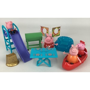 May include: A Peppa Pig playset featuring four plastic pig figures, a blue slide, a green table, a blue dining table with place settings, a gold sandcastle, a blue armchair, and a red canoe. The figures include one in a blue shirt, one in a red floral shirt, and two in orange and red outfits.