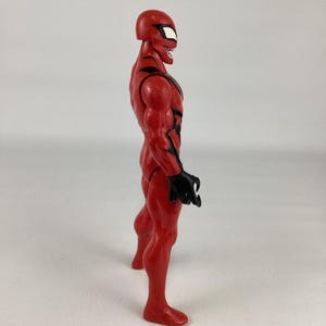 Puede incluir: Figura de acci&oacute;n roja de un superh&eacute;roe con detalles negros y una m&aacute;scara con ojos blancos. La figura tiene una musculatura, manos negras en forma de garra y una expresi&oacute;n amenazante. Vista de perfil.