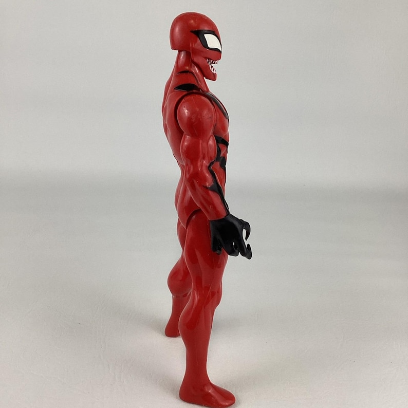 Puede incluir: Figura de acci&oacute;n roja de un superh&eacute;roe con detalles negros y una m&aacute;scara con ojos blancos. La figura tiene una musculatura, manos negras en forma de garra y una expresi&oacute;n amenazante. Vista de perfil.