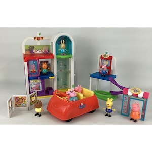 May include: A Peppa Pig playset with a red car, a multi-level building with an elevator, and character figurines. The set includes a shop, a slide, and other interactive elements, designed for imaginative play and fun.
