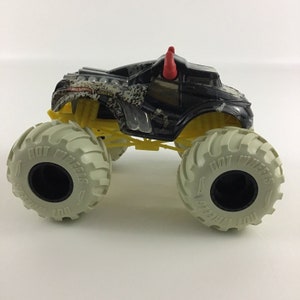 May include: Black and grey Hot Wheels Monster Truck with red horns and yellow suspension. The truck has a camouflage pattern and the words "Hot Wheels" on the tires.