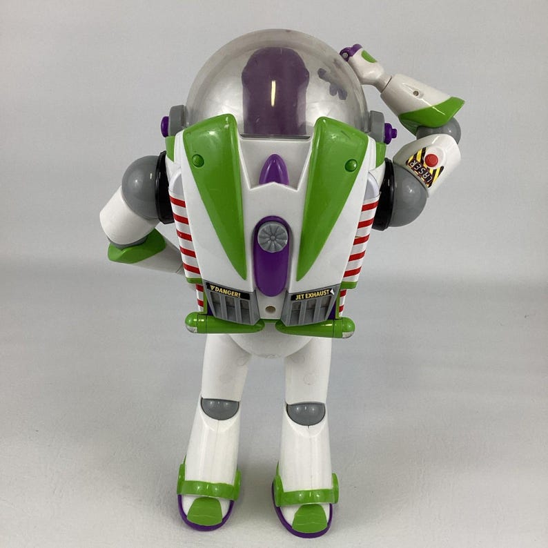 May include: A Buzz Lightyear action figure, featuring a white body with green and purple accents. The toy has a clear helmet, red and white striped wings, and the words "JET EXHAUST" and "DANGER" printed on the back.