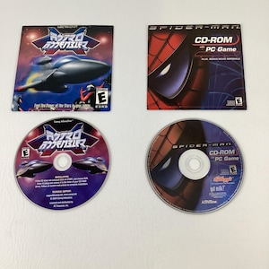May include: Two PC game CD-ROMs and their corresponding square paper inserts. One set features the game Rayxanber III with a dark space theme, while the other set features Spider-Man with a red and blue webbed mask graphic and text.
