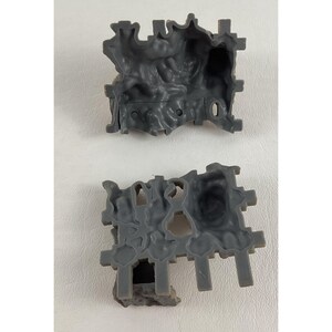 Puede incluir: Dos componentes de construcci&oacute;n de juguetes de pl&aacute;stico gris. Cada pieza tiene un dise&ntilde;o texturizado, similar a una cueva, con bordes irregulares y soportes salientes. Las piezas est&aacute;n dise&ntilde;adas para entrelazarse, lo que sugiere un tema de construcci&oacute;n o juego.