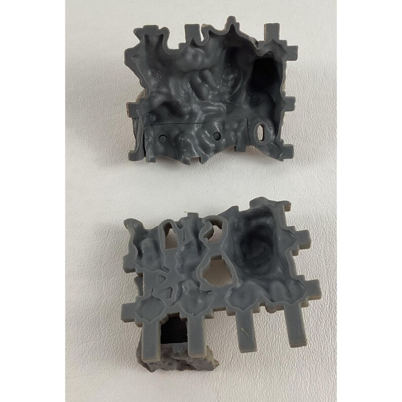 Puede incluir: Dos componentes de construcci&oacute;n de juguetes de pl&aacute;stico gris. Cada pieza tiene un dise&ntilde;o texturizado, similar a una cueva, con bordes irregulares y soportes salientes. Las piezas est&aacute;n dise&ntilde;adas para entrelazarse, lo que sugiere un tema de construcci&oacute;n o juego.