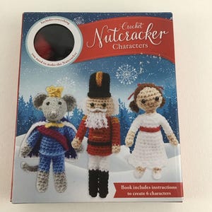 May include: A book titled "Crochet Nutcracker Characters" with a blue background and snowflakes. The cover features three crocheted figures: a mouse king, a nutcracker soldier, and a young girl. The book includes instructions to create six characters.