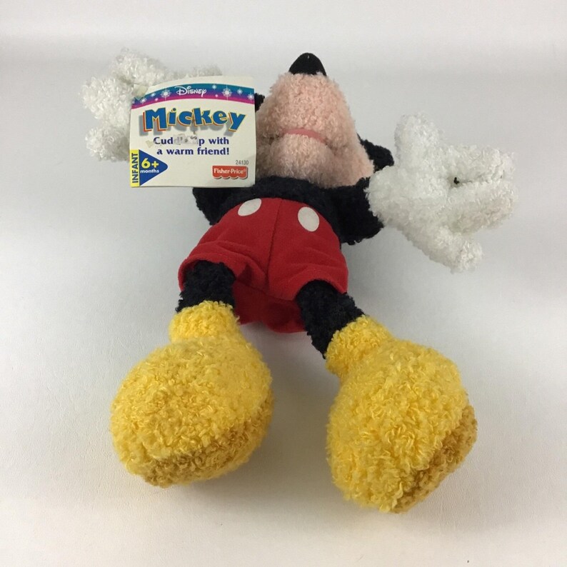May include: A plush Mickey Mouse toy with a tag that reads "Mickey Cuddle up with a warm friend!" The toy has a black head and body, red shorts with white buttons, yellow feet, and white hands. The toy is designed for infants 6+ months.