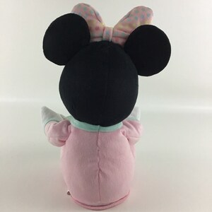 Op de afbeelding: Een pluche speelgoed van Minnie Mouse met een roze en blauwe outfit met een stippen strik. Het speelgoed zit met zijn armen uitgestrekt.