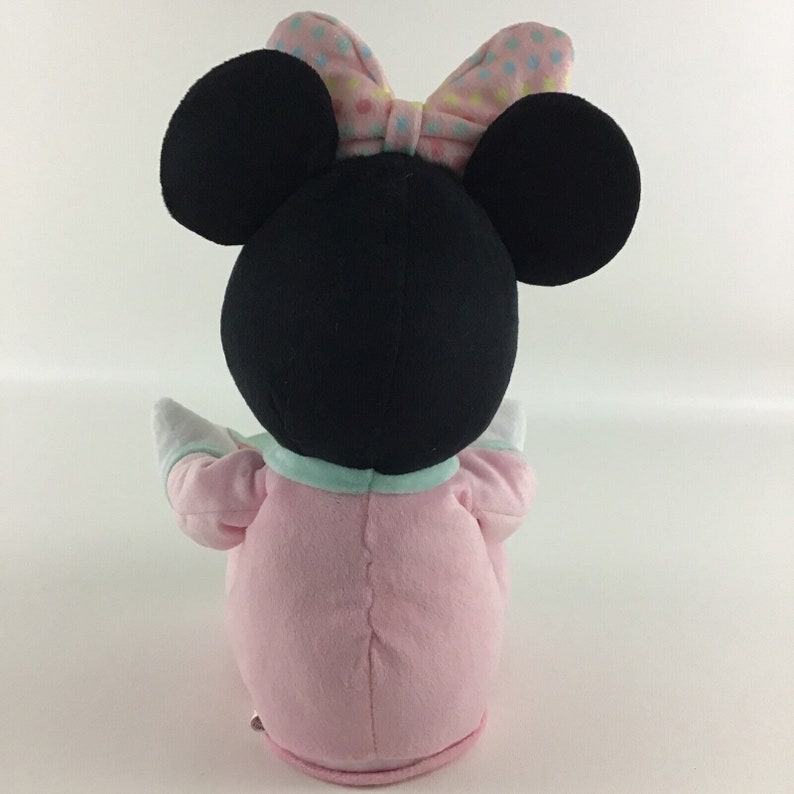 Op de afbeelding: Een pluche speelgoed van Minnie Mouse met een roze en blauwe outfit met een stippen strik. Het speelgoed zit met zijn armen uitgestrekt.