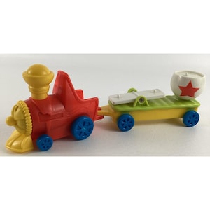 May include: A brightly coloured toy train with a red engine, yellow details, and blue wheels. The carriage is yellow and green, with a white xylophone and a white ball with a red star. A fun toy for children.