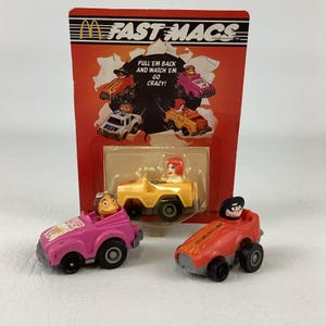 Puede incluir: Un juego de juguetes Fast Macs de McDonald's vintage con coches retráctiles en miniatura. El juego incluye un coche rosa, un jeep amarillo y un coche rojo, cada uno con un personaje conductor. El embalaje dice "Pull 'em back and watch 'em go crazy!"
