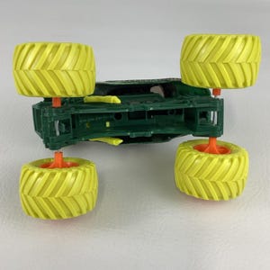 Pu&ograve; includere: Un monster truck giocattolo verde con quattro grandi pneumatici gialli. I pneumatici hanno un motivo a coste. Le ruote del camion sono attaccate con supporti arancioni.