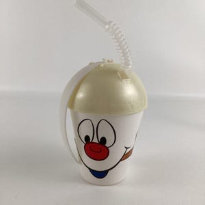 May include: White plastic cup with a cartoon face and a straw. The face has large eyes, a red nose, and a brown mustache. The cup has a white lid.