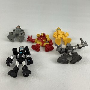 May include: A collection of five toy action figures in various colors. The figures include Iron Man in red and yellow, a silver and black figure, a yellow figure, and two gray figures. The toys are on a white surface.