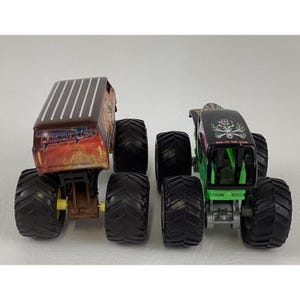 May include: Two toy monster trucks. One truck is brown and orange with the text "Thunder Bus". The other truck is black and green with a skull and crossbones design. Both trucks have large black tires.