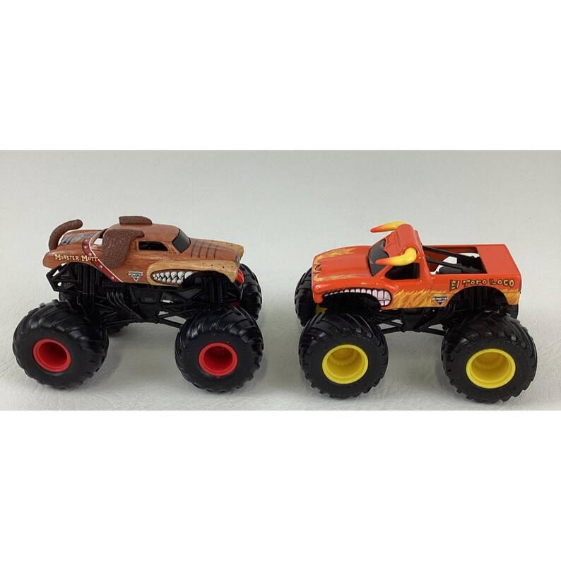 May include: Two toy monster trucks. One is brown with a dog-like design, the other is orange with a bull design. Both have large black tyres with red and yellow accents.