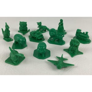 Könnte beinhalten: Eine Sammlung grüner Kunststoff-Spielsteine, darunter Tierfiguren wie Känguru, Eule, Katze, Löwe und Affe, sowie ein Zug, ein Auto, ein Flugzeug und eine menschliche Figur. Die Teile liegen auf einer weißen Oberfläche.