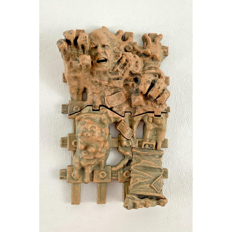 Puede incluir: Escultura en relieve marr&oacute;n detallada con apariencia desgastada. La obra de arte representa una figura humana angustiada y otros elementos abstractos. La escultura est&aacute; montada sobre una superficie blanca.