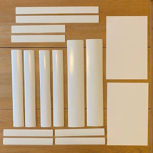 Op de afbeelding: Een set witte kunststof trimstukken voor meubels, inclusief rechte en gebogen stukken. De trimstukken zijn gerangschikt op een houten oppervlak.
