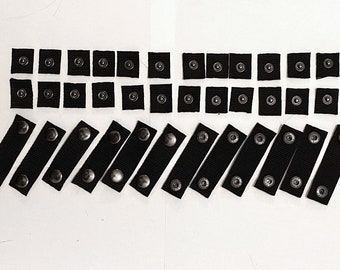 May include: A set of black snap fasteners, some are individual snaps and some are attached to black straps.