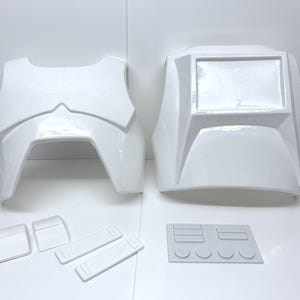 Op de afbeelding: Witte plastic pantseronderdelen, waaronder een borstplaat, rugplaat, schouderstukken en andere componenten. Het pantser heeft een glanzende afwerking en lijkt nieuw te zijn. De stukken zijn gerangschikt op een wit oppervlak, wat wijst op een cosplay- of kostuumset.