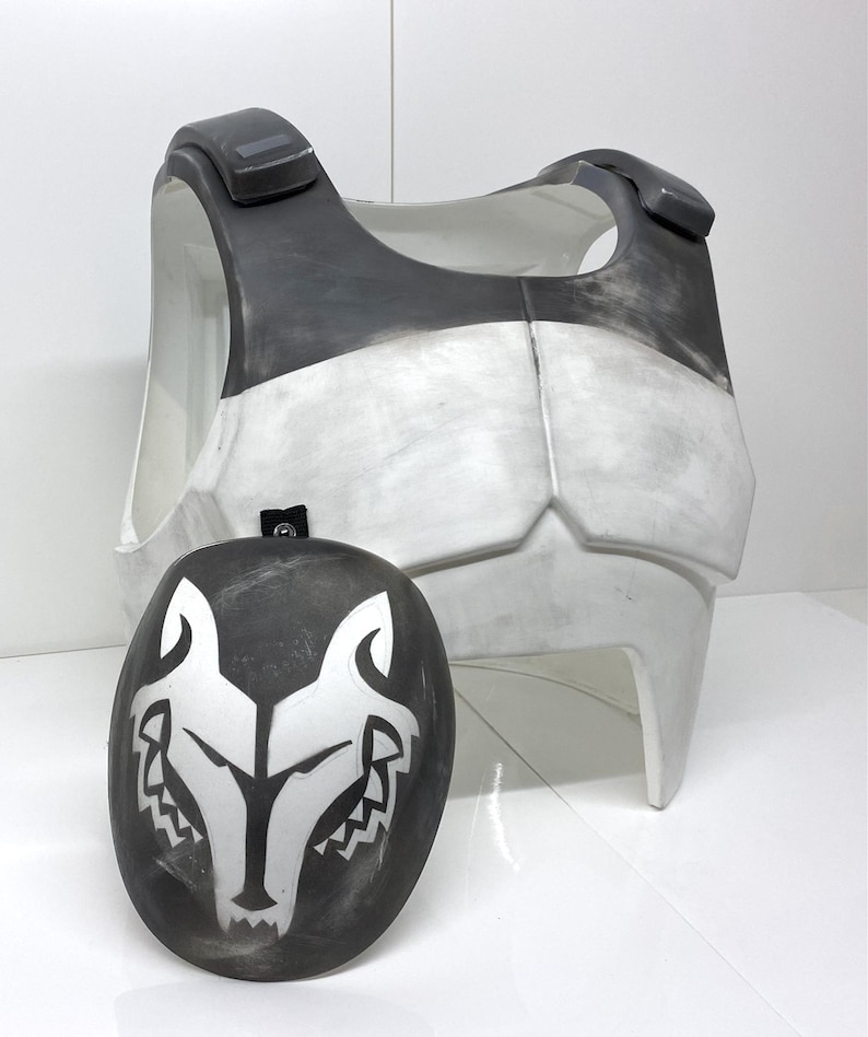 Op de afbeelding: Een tweedelige kostuumset met een borstplaat en een masker. De borstplaat is voornamelijk wit met grijze accenten, terwijl het masker zwart is met een wit wolfsontwerp. De set is waarschijnlijk bedoeld voor cosplay of kostuums.