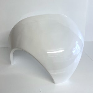Può includere: Scultura bianca, liscia, curva e cava, realizzata in un materiale duro e lucido. Assomiglia a un'opera d'arte moderna o a un design futuristico.