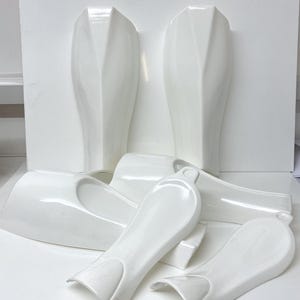 May include: Set of six white plastic shin guards for sports, featuring a sleek, modern design.