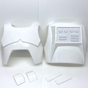 Op de afbeelding: Witte plastic pantseronderdelen, waaronder een borstplaat, een rugplaat en kleinere componenten. De borstplaat heeft een kenmerkende vorm met een verhoogd middengedeelte. De rugplaat heeft een rechthoekig paneel met cirkelvormige en rechthoekige details.