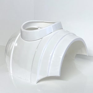 Puede incluir: Armadura de hombro de plástico blanco para disfraz con un borde elevado alrededor de la abertura del cuello.