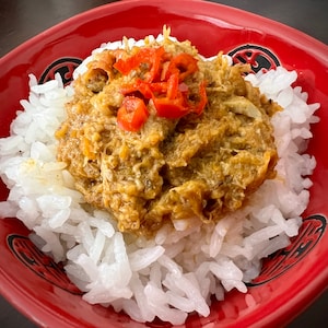 May include: A red bowl filled with white rice topped with a brown meat sauce and red chili peppers.