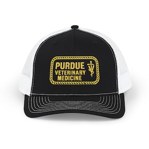 May include: A black and white trucker cap with a curved peak. The front panel displays a gold rectangular emblem with the text "PURDUE VETERINARY MEDICINE" and a caduceus symbol. The cap has a white mesh back and a black peak with white stitching.