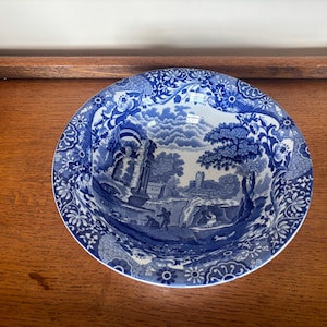 May include: A round ceramic bowl featuring a blue and white transferware pattern. The design depicts a detailed landscape with architectural ruins, trees, and figures, surrounded by a wide border of intricate floral and scroll motifs.