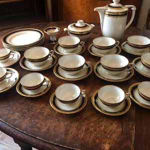 Puede incluir: Un juego de té vintage con ribetes dorados y negros. El juego incluye una tetera, un azucarero, una jarra de crema y 12 tazas de té y platillos.