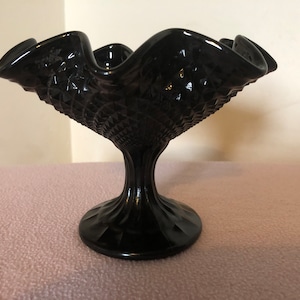 K&ouml;nnte beinhalten: Eine schwarze Glasschale auf einem Sockel mit einem gewellten Rand und einem Diamantenmuster. Die Schale steht auf einem Sockel mit einem geriffelten Design.