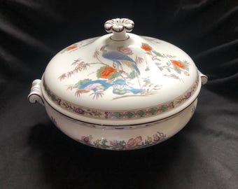 May include: White ceramic serving dish with lid, featuring a colorful bird and floral design. The dish has a decorative rim and a floral knob on the lid. The handles are curved.